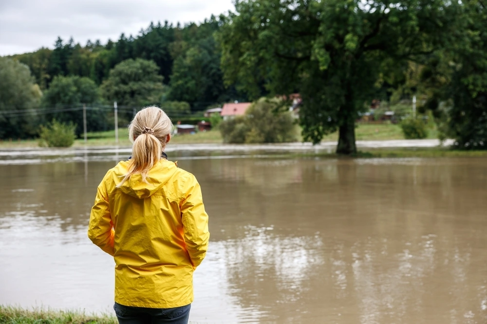 Eine Frau in einem gelben Regenmantel steht am Ufer eines Flusses.
