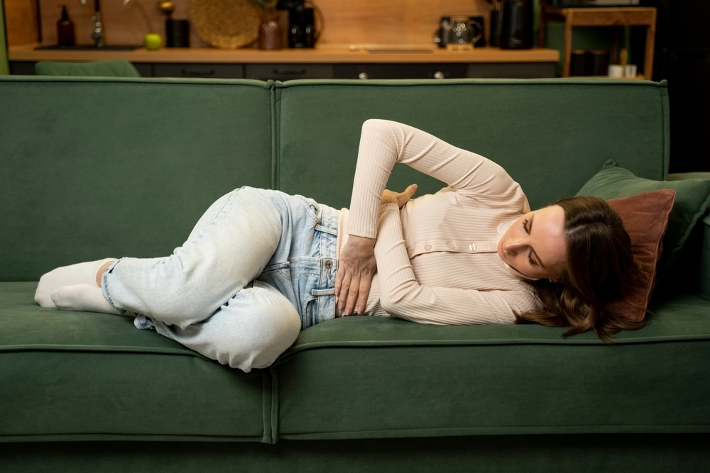 Eine Frau liegt auf einem Sofa und hält sich den Bauch vor Schmerzen.